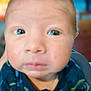 baby, close_up, face, indoor, child, expression, blue_clothing, person, head, eyes, skin, newborn, portrait, blurred_background, furniture, hand, young, infant, cute, serious