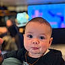 Rafael a rejoint le concours — aidez-le/la à gagner de superbes lots ! baby, infant, child, face, eyes, necklace, black_clothing, indoor, person, curious_expression, chubby_cheeks, portrait, close_up, adult_arm, background_blur, colorful_lights, sitting, cute, young_child, casual