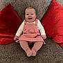 Mabel-Ivy is registered to the contest to win money with this photo: baby, child, smiling, pink_dress, tights, couch, red_cushions, indoor, portrait, happy, seated, infant, home, furniture, cute, person, cozy, living_room, textile, comfort