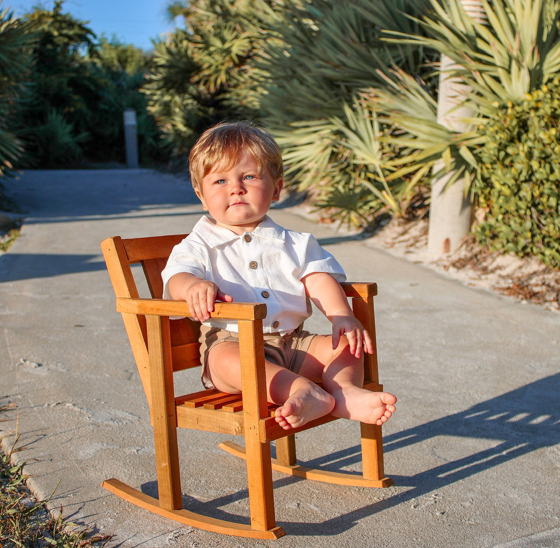 Krew is registered to the contest to win money with this photo: arecales, baby, baby_toddler_clothing, chair, child, comfort, fun, grass, leisure, outdoor_furniture, palm_tree, person, plant, recreation, shorts, sitting, sky, toddler, tree, vacation