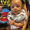 Amiyah is registered to the contest to win money with this photo: baby, infant, person, child, clothing, bib, hand, face, eyes, sitting, holding, blanket, colorful, curious, cute, indoor, portrait, skin, expression, young