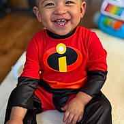 Joseph joined the competition — help win amazing prizes! toddler, child, smiling, happy, superhero_costume, red_clothing, black_clothing, indoor, toy, blurred_background, sitting, portrait, cute, baby, person, face, hand, footwear, wooden_floor, home