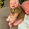 baby, child, infant, smiling, happy, sitting, portrait, face, eyes, short_hair, onesie, clothing, bare_feet, blanket, pillow, couch, sofa, living_room, indoor, cozy