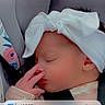 baby, sleeping, infant, car_seat, bow, headband, white_clothing, portrait, face, closed_eyes, indoors, vehicle, seatbelt, blanket, hand, peaceful, lock_screen, smartphone_screenshot, notifications, close_up