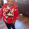 Braylon is registered to the contest to win money with this photo: toddler, child, indoors, mickey_mouse, hoodie, pacifier, smiling, standing, floor, living_room, couch, sunlight, window, clothing, socks, person, happy, young_child, home, casual
