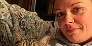 Archie is registered to the contest to win money with this photo: woman, cat, tabby_cat, indoor, hoodie, couch, blanket, window, curtain, pet, face, portrait, cozy, relaxed, whiskers, paw, feline, human, casual, smile