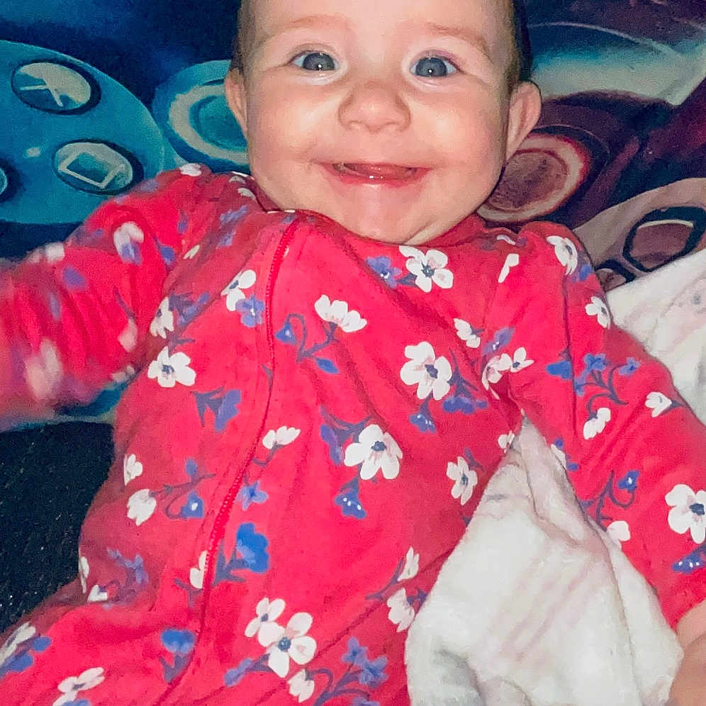 Nicole joined the competition — help win amazing prizes! baby, blanket, blue_eyes, child, colorful, comfort, cozy, cushion, cute, fabric, face, floral_pattern, happy, indoor, infant, lying_down, onesie, portrait, smiling, young_child