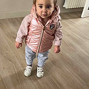 Lucia participe au concours pour gagner de l'argent avec cette photo : toddler, child, indoor, wooden_floor, pink_vest, striped_pants, white_shoes, curly_hair, pigtails, radiator, flooring, wall, door, standing, casual_clothing, young_child, portrait, looking_up, curious, home