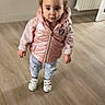 toddler, child, indoor, wooden_floor, pink_vest, striped_pants, white_shoes, curly_hair, pigtails, radiator, flooring, wall, door, standing, casual_clothing, young_child, portrait, looking_up, curious, home