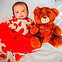 baby, infant, child, teddy_bear, stuffed_animal, bed, white_bedding, pillow, hearts_pattern, red_tutu, pajamas, cozy, cute, portrait, smiling_face, plush, toy, lying_down, soft_texture, nursery