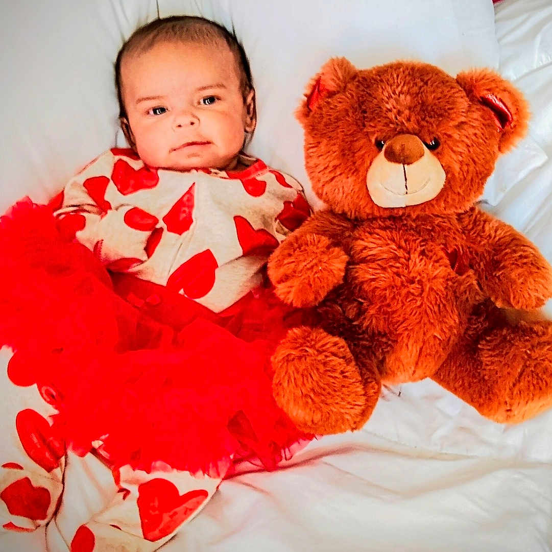 Phelloni is registered to the contest to win money with this photo: baby, bed, child, cozy, cute, hearts_pattern, infant, lying_down, nursery, pajamas, pillow, plush, portrait, red_tutu, smiling_face, soft_texture, stuffed_animal, teddy_bear, toy, white_bedding