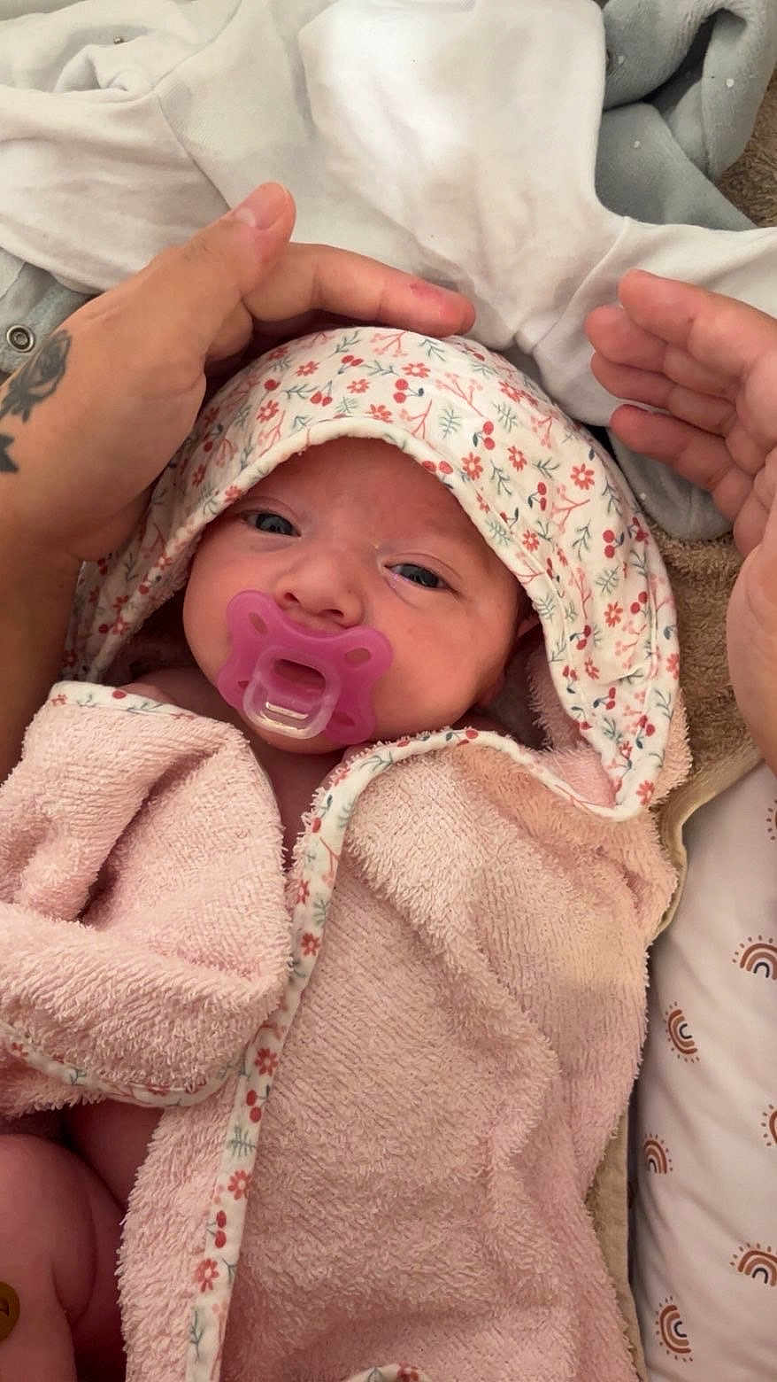 Taïsiana a rejoint le concours — aidez-le/la à gagner de superbes lots ! baby, infant, pacifier, pink_towel, floral_pattern, tattoo, hands, close_up, wrapped, cozy, sleepy, cute, newborn, soft_texture, blanket, person, face, skin, indoor, comfort