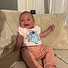 baby, cartoon_shirt, child, clothing, comfortable, corduroy, couch, cute, face, happy, home, indoor, infant, joyful, person, pillow, pink_pants, relaxed, sitting, smiling