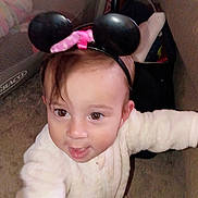 Jayda is registered to the contest to win money with this photo: baby, child, infant, portrait, face, eyes, smiling, happy, headband, mouse_ears, pink_bow, cream_clothing, long_sleeves, sitting, indoor, couch, furniture, carpet, closeup, playful