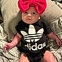 baby, infant, child, headband, bow, clothing, onesie, black_clothing, logo, adidas, bed, blanket, pillow, pattern, person, indoor, cute, face, skin, lying_down