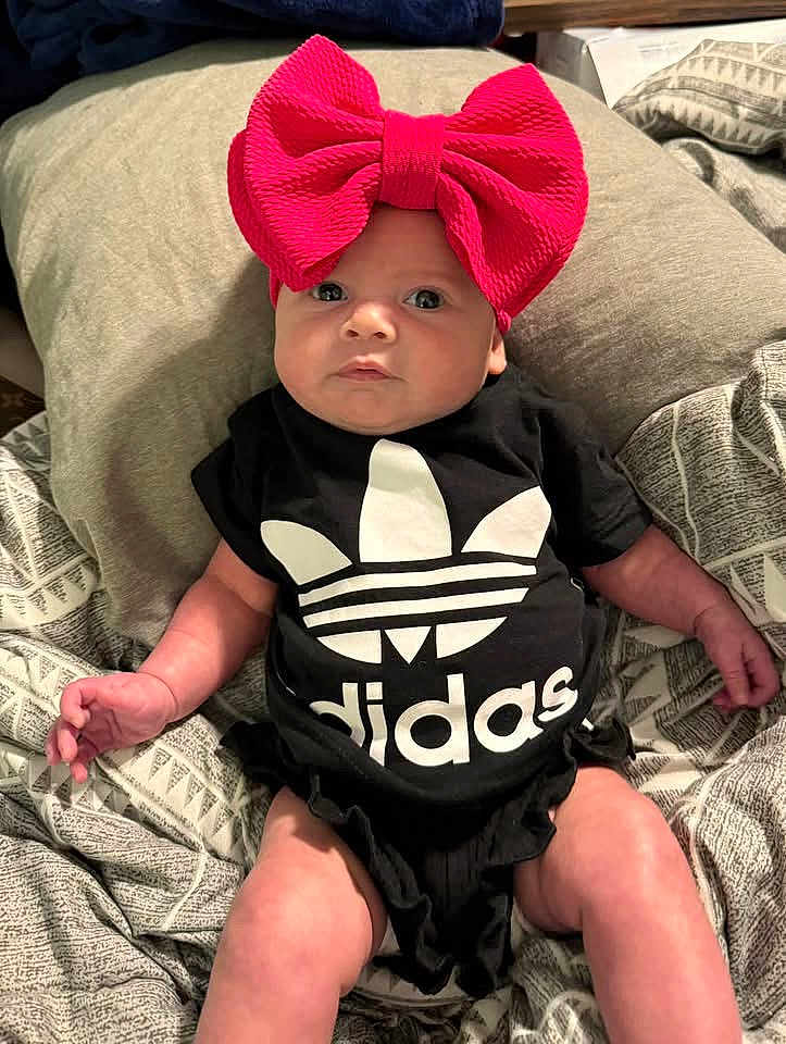 Kimberlyn joined the competition — help win amazing prizes! baby, infant, child, headband, bow, clothing, onesie, black_clothing, logo, adidas, bed, blanket, pillow, pattern, person, indoor, cute, face, skin, lying_down