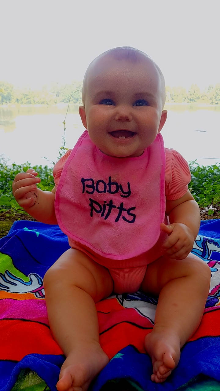 Gracelyn is registered to the contest to win money with this photo: baby_toddler_clothing, blue, cheek, face, finger, grass, happy, human_body, joy, knee, leg, leisure, mouth, people_in_nature, person, pink, plant, skin, smile, thigh