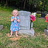 barefoot, blue_dress, casual_clothing, cemetery, child, daylight, flowers, grass, gravestone, headstone, memorial, nature, outdoor, person, playful, shrubbery, toddler, trees, water_bottle, young_child