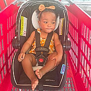 Ashiya joined the competition — help win amazing prizes! toddler, child, car_seat, shopping_cart, orange_bow, floral_outfit, black_straps, red_cart, indoor, window, sunlight, curly_hair, seat_belt, baby, cute, foot, hand, headband, safety, expression