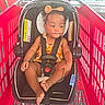 toddler, child, car_seat, shopping_cart, orange_bow, floral_outfit, black_straps, red_cart, indoor, window, sunlight, curly_hair, seat_belt, baby, cute, foot, hand, headband, safety, expression