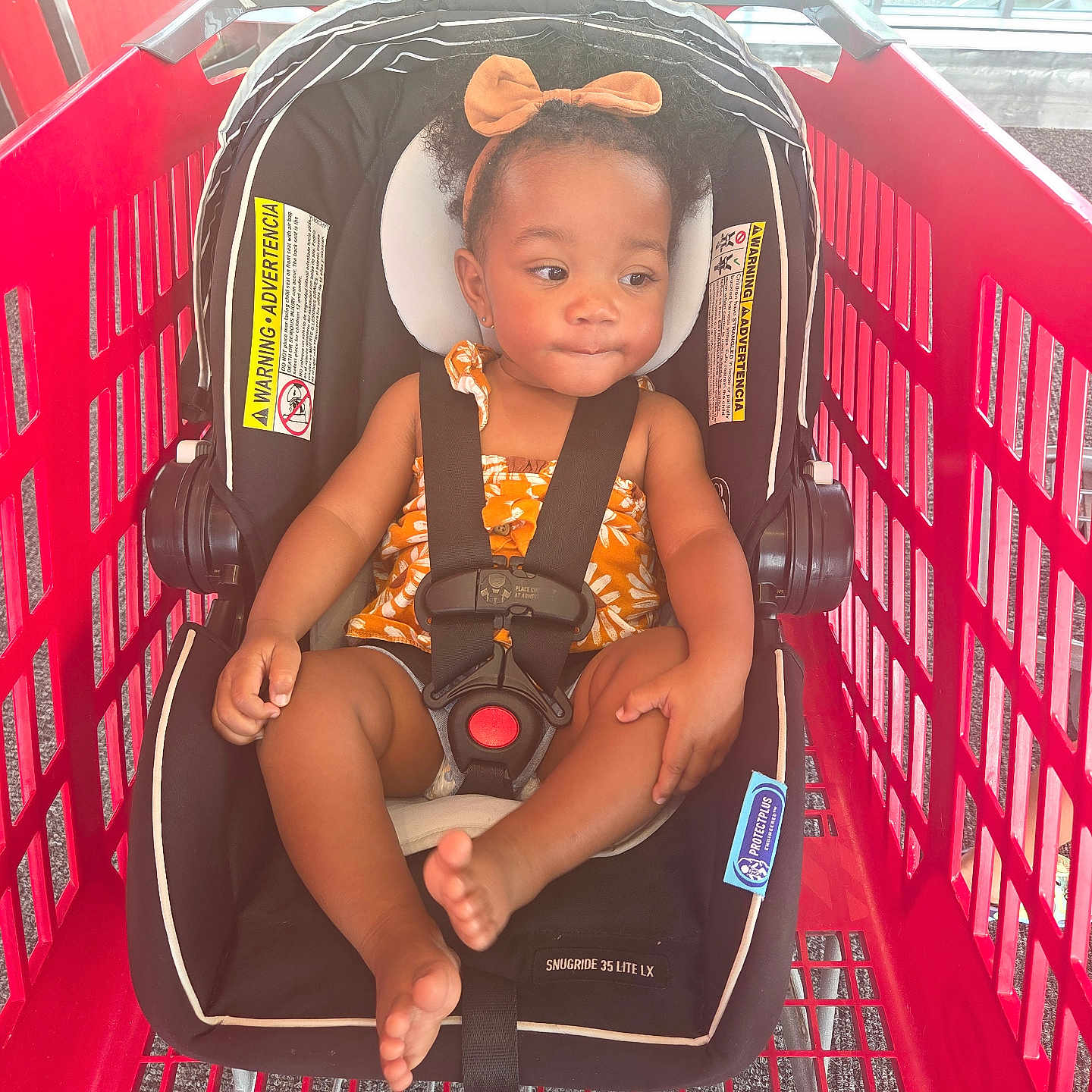 Ashiya joined the competition — help win amazing prizes! toddler, child, car_seat, shopping_cart, orange_bow, floral_outfit, black_straps, red_cart, indoor, window, sunlight, curly_hair, seat_belt, baby, cute, foot, hand, headband, safety, expression
