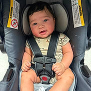 Zo joined the competition — help win amazing prizes! baby, car_seat, child, infant, seat_belt, onesie, dinosaur_pattern, smiling, happy, cute, safety, warning_label, straps, indoor, person, portrait, hands, legs, foot, head