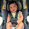 baby, car_seat, child, infant, seat_belt, onesie, dinosaur_pattern, smiling, happy, cute, safety, warning_label, straps, indoor, person, portrait, hands, legs, foot, head