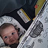 baby, infant, child, face, eyes, wide_eyed, lying_down, bassinet, car_seat, blanket, duck_toy, stuffed_animal, plush_toy, patterned_fabric, cozy, indoor, portrait, safety_label, sleeping_area, photography
