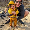 Elio participe au concours pour gagner de l'argent avec cette photo : adult, baby, barefoot, beach, bonding, casual_clothing, child, holding, hooded_sweatshirt, laughing, man, outdoor, playful, portrait, rocks, sand, smile, sunglasses, toddler, yellow_jacket