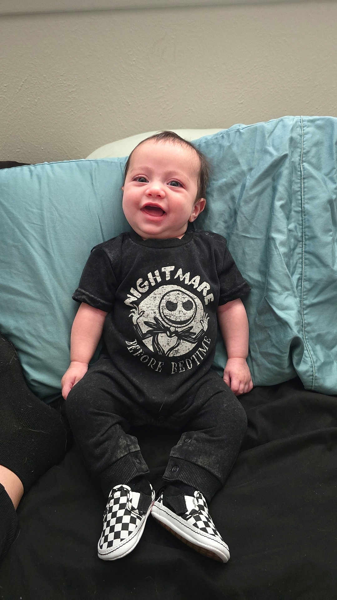 Cole is registered to the contest to win money with this photo: baby, child, smiling, sitting, black_clothing, checkered_shoes, couch, pillows, indoor, happy, infant, footwear, cute, young_child, portrait, casual_clothing, comfortable, home, person, black_background