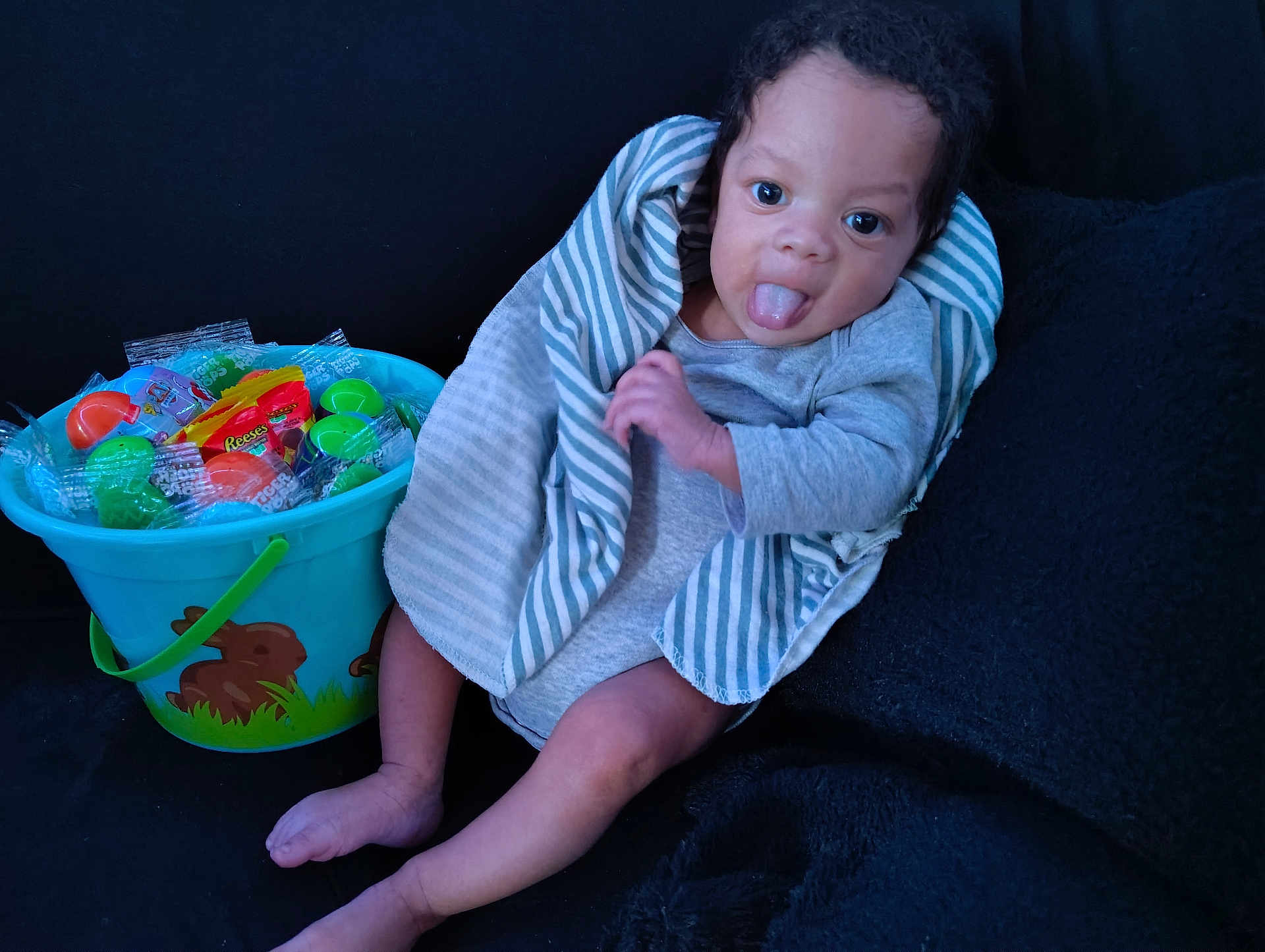 Adonyze joined the competition — help win amazing prizes! baby, child, tongue_out, striped_blanket, bucket, candy, toys, blue_bucket, gray_clothing, sitting, playful, cute, dark_background, indoor, infant, person, smiling, legs, hand, face