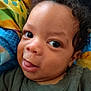 Adonyze is registered to the contest to win money with this photo: baby, closeup, face, tongue, curly_hair, green_clothing, blanket, colorful, infant, child, portrait, cute, young, expression, indoors, person, skin, head, eyes, smile