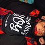 baby, infant, child, sleepwear, pajamas, red_black_plaid, black_background, shirt, text_on_clothing, face, hand, peace_sign, lying_down, cute, young_child, portrait, indoor, person, newborn, cozy