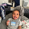 baby, blanket, child, clothing, cushion, face, furniture, happy, head, home, household, indoor, infant, laundry_basket, person, playful, seated, shirt, smiling, sticker