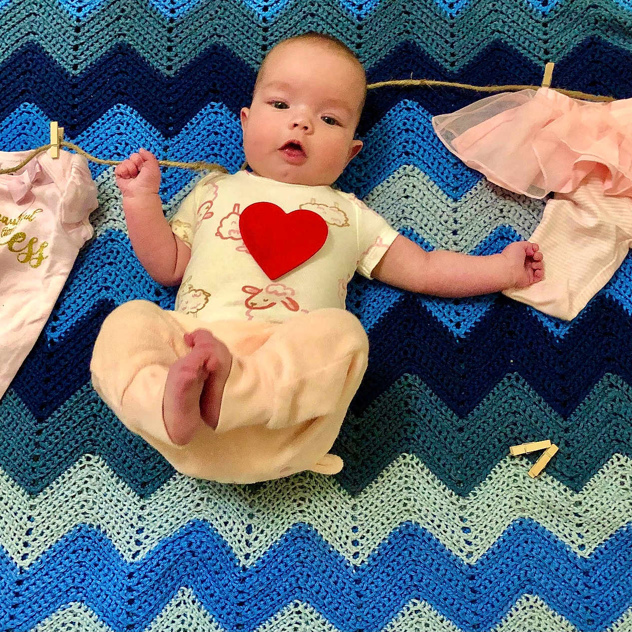 Lindy is registered to the contest to win money with this photo: baby, baby_girl, blanket, blue, child, clothesline, clothespins, clothing, crochet, cute, fabric, heart, home, infant, laying_down, pattern, pink, playful, portrait, soft