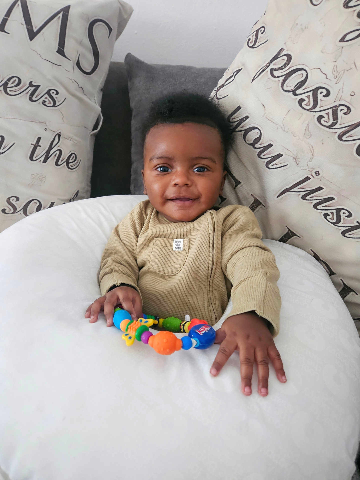 Ezra joined the competition — help win amazing prizes! baby, child, clothing, colorful, cozy, cushion, cute, face, hand, happy, home, indoor, infant, person, pillow, playful, portrait, seated, smile, toy