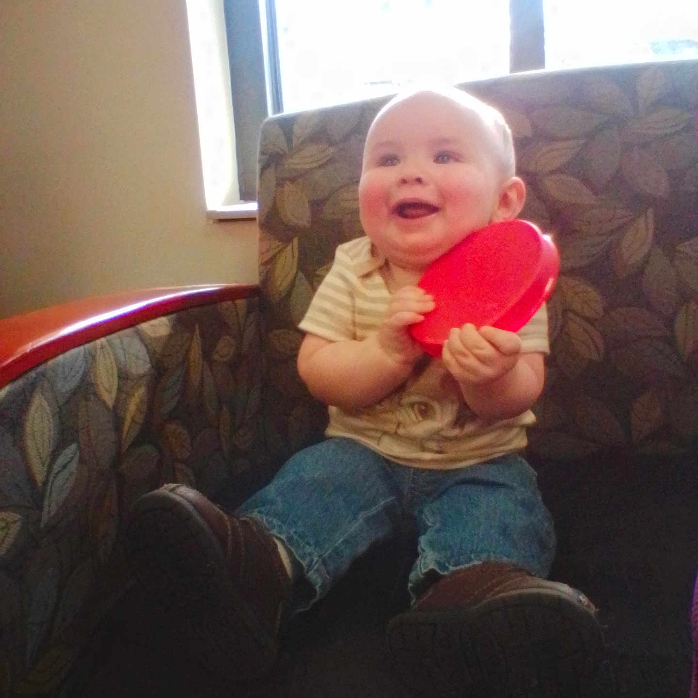 Ascher is registered to the contest to win money with this photo: armchair, baby, child, clothing, cute, face, happy, indoor, infant, jeans, person, playful, red, seated, shoes, smile, striped_shirt, sunlight, toy, window