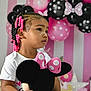balloons, birthday_party, black, celebration, child, curly_hair, cute, hair_beads, holding, indoor, minnie_mouse, party_decorations, pink, plush_toy, polka_dots, portrait, side_profile, toddler, white_shirt, young_child