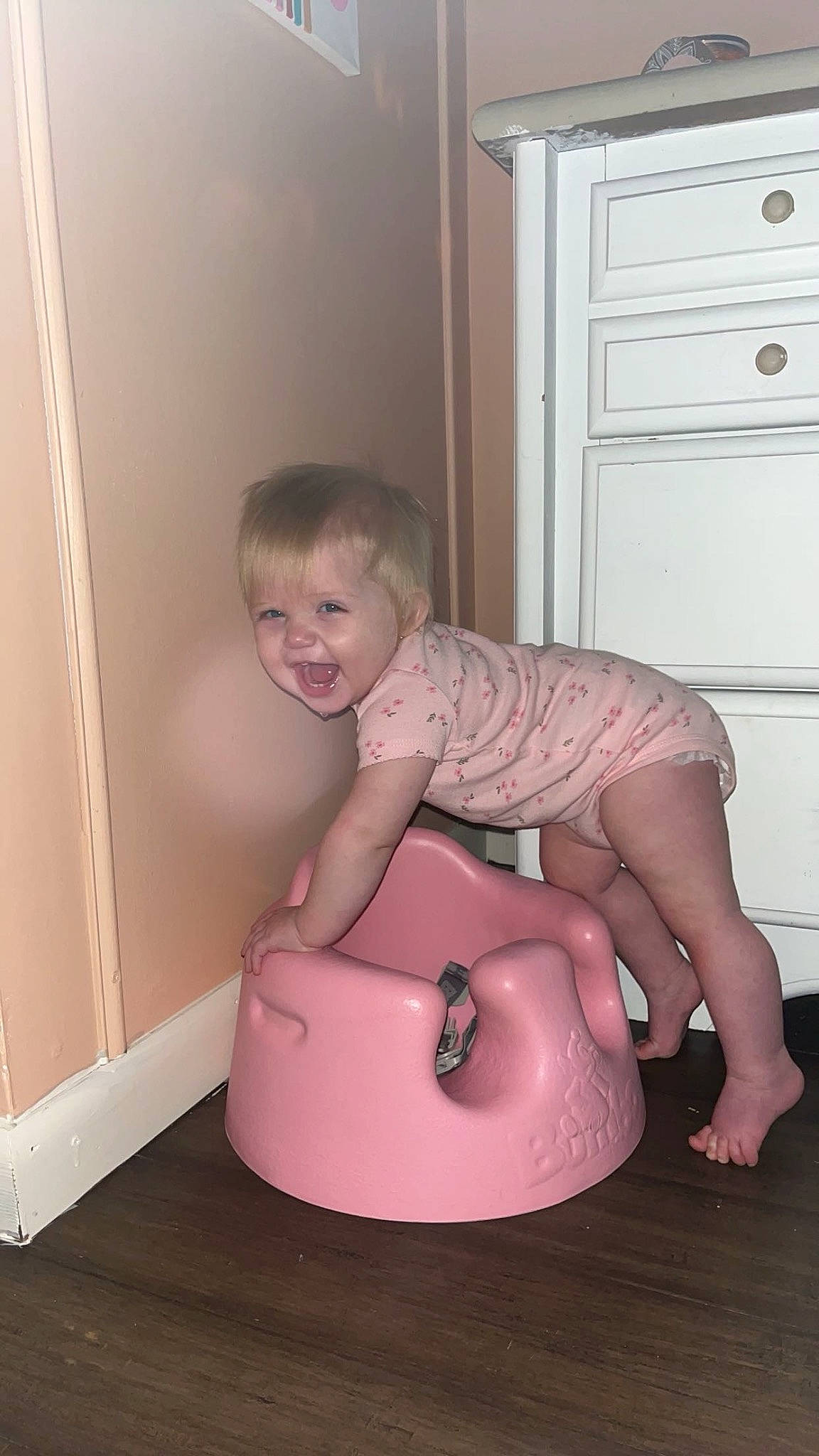 Lillian is registered to the contest to win money with this photo: baby, baby_toddler_clothing, cabinetry, chest_of_drawers, child, cupboard, drawer, dresser, floor, flooring, fun, hardwood, human_leg, knee, magenta, person, pink, sitting, smile, toddler