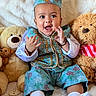 baby, child, teddy_bear, plush_toy, blue_outfit, hat, smiling, sitting, clapping, cute, soft_blanket, indoors, portrait, happy, infant, white_socks, decorative_clothing, toy, close_up, face