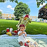 balloons, bananas, blanket, cap, celebration, child, clouds, drink, fruit, grass, outdoor, picnic, shoes, sky, snacks, strawberries, toddler, toy, tree, watermelon