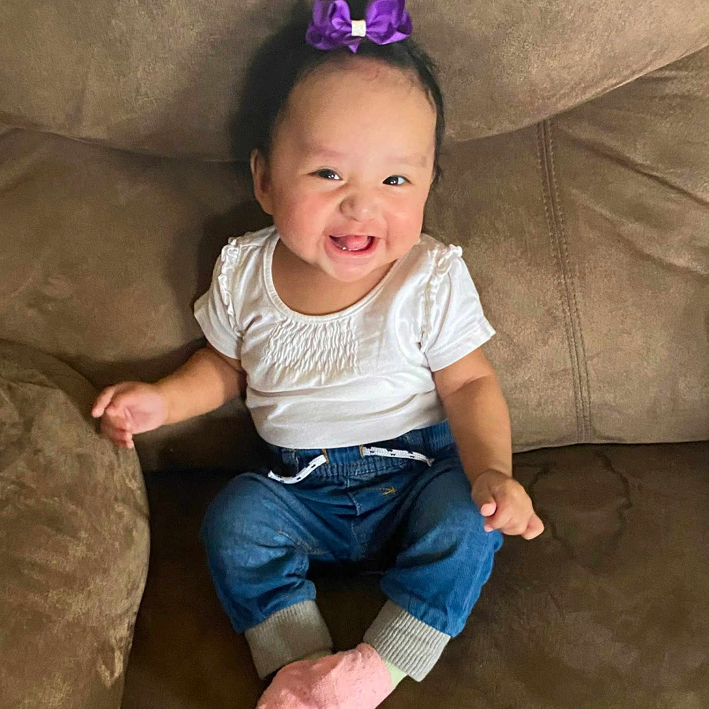 Lydia joined the competition — help win amazing prizes! baby, child, smiling, sitting, portrait, indoors, couch, furniture, purple_bow, white_shirt, blue_jeans, pink_socks, happy, infant, face, arms, hands, home, fashion, photography