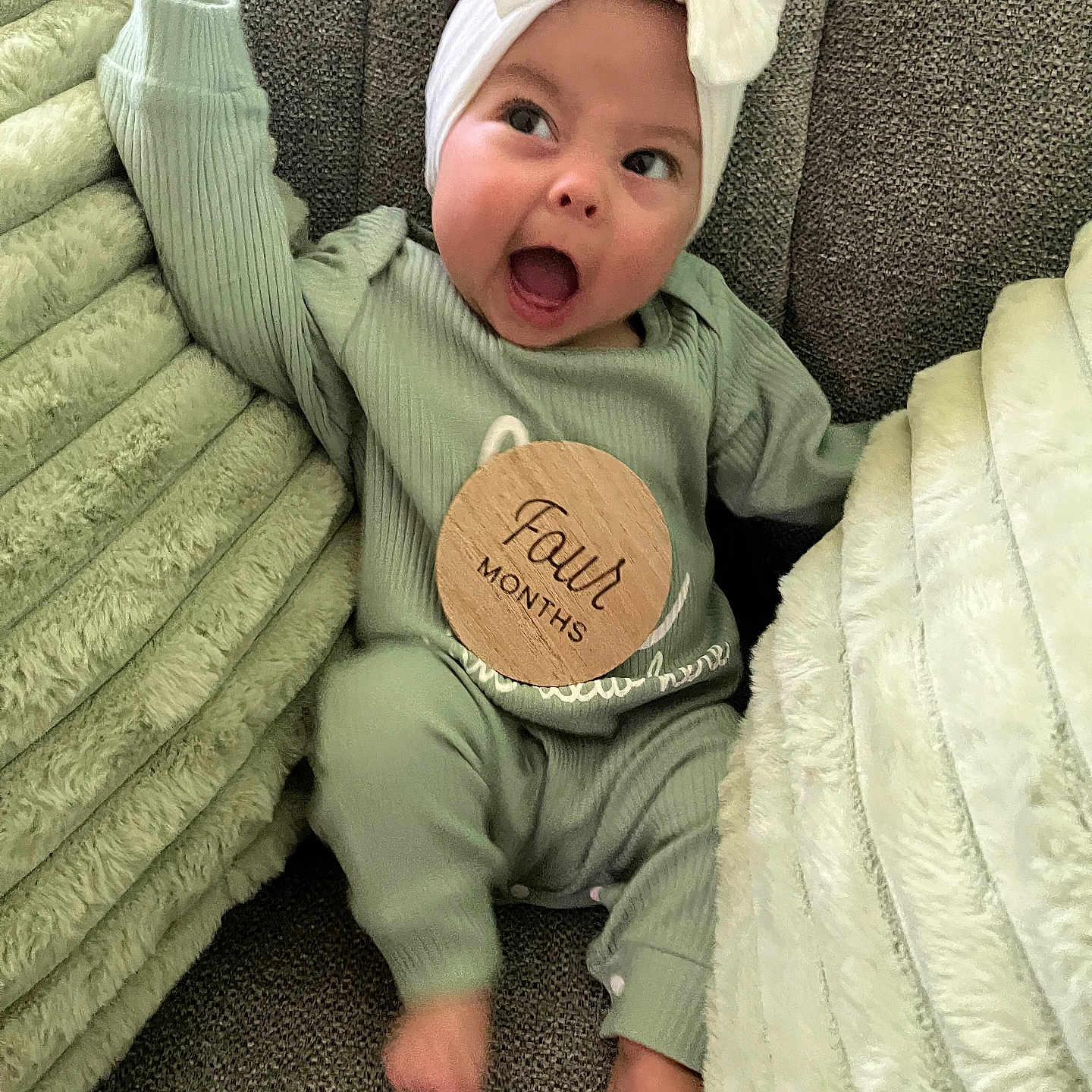 Hyacinth is registered to the contest to win money with this photo: baby, blanket, bow, child, couch, cozy, cute, expression, four_months, green_outfit, happy, headband, indoor, infant, person, portrait, sitting, smiling, soft_texture, young_child
