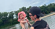 Hyacinth is registered to the contest to win money with this photo: baby, adult, lake, water, trees, outdoor, nature, smiling, hat, tattoo, chair, person, happy, summer, sky, cloudy, family, holding, casual, relaxation