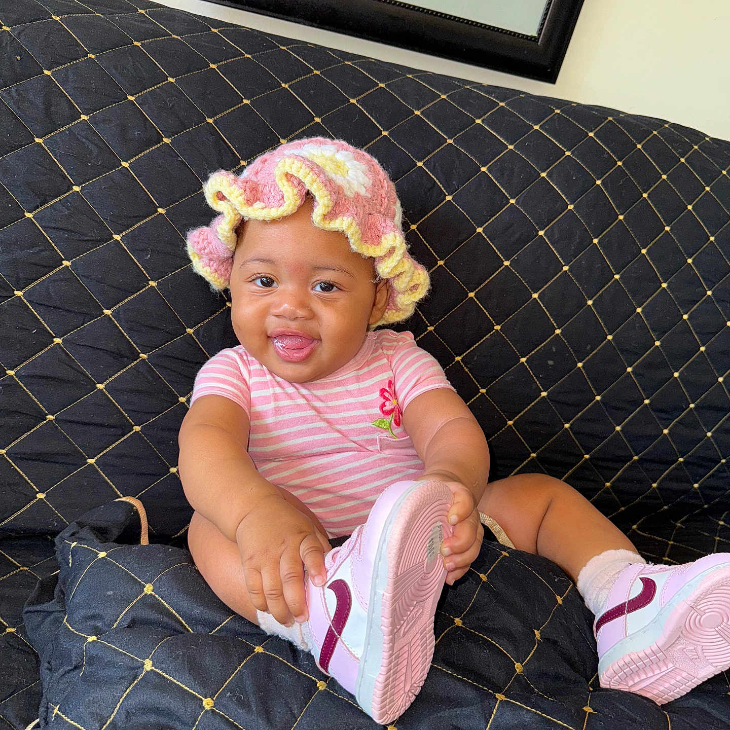Jnijah joined the competition — help win amazing prizes! baby, black_quilted_couch, child, couch, crocheted_hat, cute, footwear, happy, home, indoor, infant, person, pink_hat, playful, portrait, shoe, sitting, smiling, striped_onesie, tongue_out