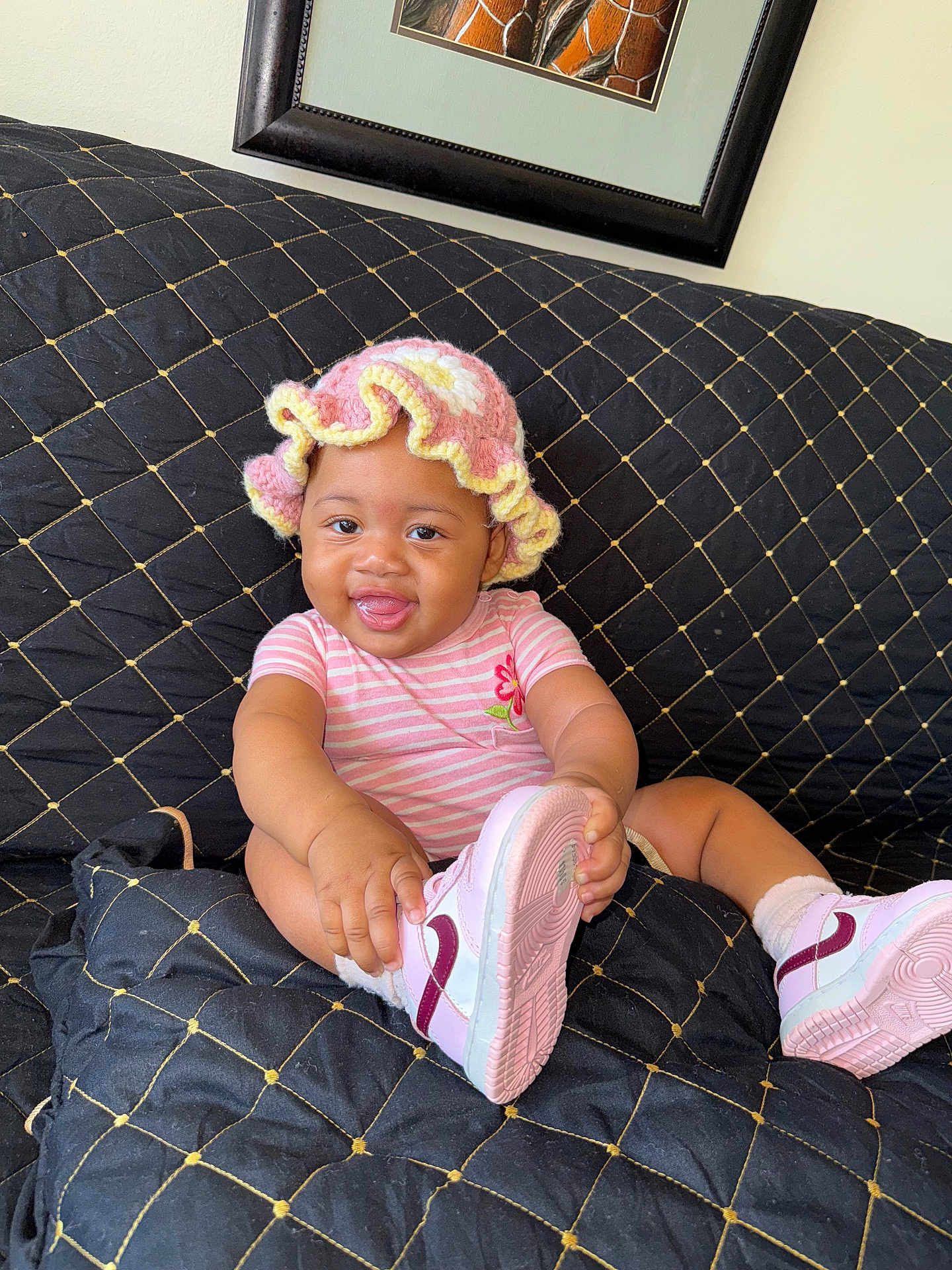 Jnijah joined the competition — help win amazing prizes! baby, child, smiling, pink_hat, striped_onesie, shoe, couch, black_quilted_couch, cute, happy, indoor, playful, sitting, tongue_out, crocheted_hat, footwear, infant, person, portrait, home