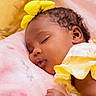 baby, sleeping, yellow_clothing, blanket, pink_blanket, balloon, face, infant, peaceful, curly_hair, hand, closeup, portrait, soft_texture, indoor, child, cute, resting, yellow_bow, newborn