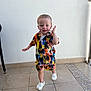toddler, child, smiling, standing, colorful_clothing, tropical_pattern, shorts, shirt, white_crocs, indoor, tile_floor, wall, playful, happy, cute, person, young_child, casual, summer_wear, footwear
