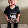 toddler, child, smiling, standing, black_shirt, ultrasound, baby_picture, big_brother, indoor, blanket, happy, blue_eyes, short_hair, pants, socks, person, portrait, announcement, cute, joyful