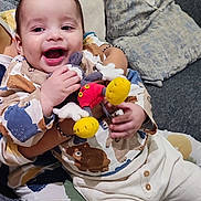 Yassin a rejoint le concours — aidez-le/la à gagner de superbes lots ! baby, child, clothing, comfort, couch, cushion, cute, face, hand, happy, home, indoor, infant, patterned_clothes, person, plush_toy, sitting, smiling, toy, warmth